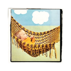 May include: A baby in a yellow and brown crocheted hammock with fringe. The hammock is hanging from a blue sky background with white clouds.