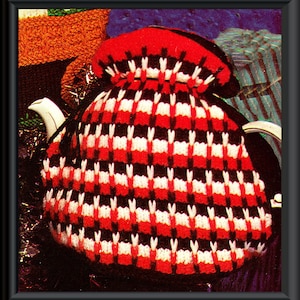 Puede incluir: Un calienta-tetera de punto de crochet rojo, blanco y negro con un patrón a cuadros. El calienta-tetera está diseñado para adaptarse a una tetera estándar.