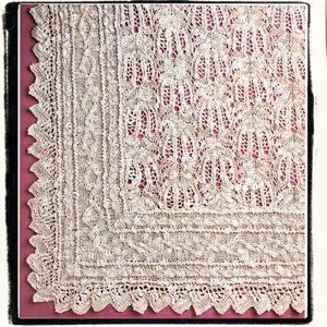 May include: A close-up of a white crocheted shawl with a delicate lace pattern. The shawl has a scalloped edge and is made with a fine yarn.