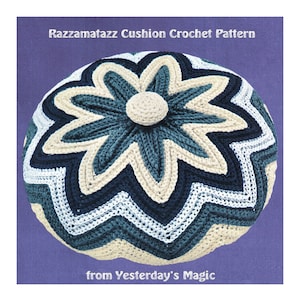 Puede incluir: Un cojín tejido a crochet en forma de flor con un botón en el centro. El cojín está hecho en tonos de azul, blanco y crema. El texto "Razzamatazz Cushion Crochet Pattern from Yesterday's Magic" está impreso debajo del cojín.