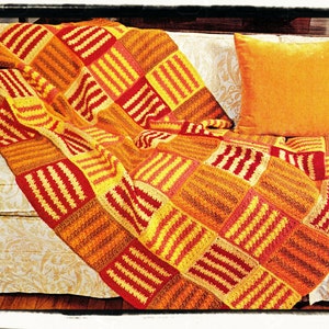 May include: A crocheted throw blanket in shades of orange, yellow, and red, with a striped pattern. The blanket is draped over a white couch with a matching orange pillow.