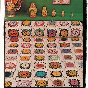 May include: A crocheted blanket with a white background and colorful floral designs. The blanket is made up of squares with a raised flower design in the center of each square. The blanket is folded in half and the top half is resting on a green surface.