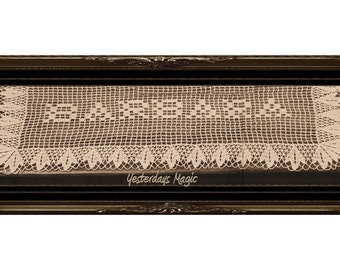 May include: A delicate, off-white crocheted lace tablecloth with a scalloped edge and a repeating pattern of small squares. The tablecloth is displayed in a dark wood frame with the text "Yesterdays Magic" at the bottom.