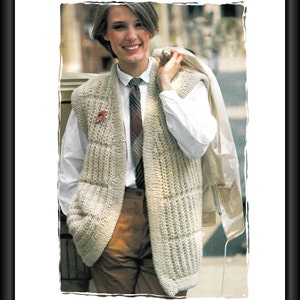 May include: A woman wearing a white shirt with a patterned tie, a beige knitted vest, and brown pants. She is holding a white jacket over her shoulder.