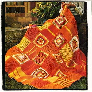 May include: A large crocheted blanket with a patchwork design in shades of orange, yellow, and white. The blanket is made up of squares with different patterns, including flowers and stripes.