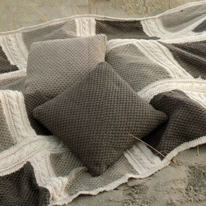 May include: A knitted throw blanket with a cable knit pattern in beige and brown. Two matching knitted pillows are on top of the blanket.