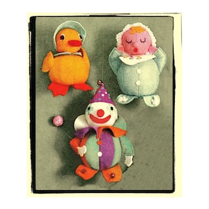 Può includere: Un'immagine vintage con tre giocattoli di stoffa fatti a mano: un'anatra arancione con un cappello blu, una bambola in un vestito blu e un clown con un vestito viola e verde. Una palla rosa è appesa vicino al clown.