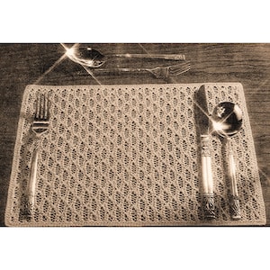 Puede incluir: Primer plano de una cubertería con un tenedor, un cuchillo y una cuchara de plata sobre un mantel individual de crochet beige.