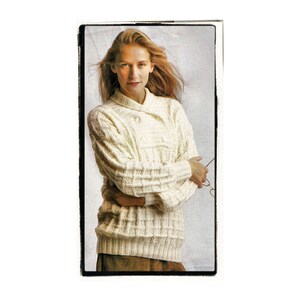 May include: A white knitted sweater with a double breasted closure and a collar. The sweater has a cable knit pattern.