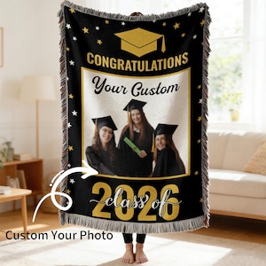 Op de afbeelding: Zwarte afstudeer plaid met gouden tekst en accenten. De plaid heeft de woorden "CONGRATULATIONS" en "class of 2026", samen met een foto van drie afgestudeerden. De plaid heeft een gefranjerde rand en een sterrenpatroon.