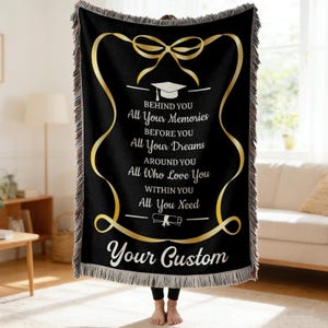 Op de afbeelding: Zwarte geweven sprei met gouden tekst en accenten. De tekst luidt: "BEHIND YOU All Your Memories BEFORE YOU All Your Dreams AROUND YOU All Who Love You WITHIN YOU All You Need Your Custom". De sprei heeft een afstudeerthema.