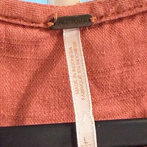 Puede incluir: Primer plano de una prenda de color coral con una etiqueta que dice "Free People". La etiqueta tambi&eacute;n indica que la prenda fue fabricada en Indonesia. La prenda est&aacute; colgada en una percha negra.