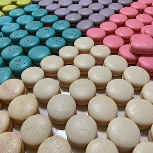 May include: A colorful assortment of macarons arranged in rows. The macarons are in various colors, including blue, pink, purple, yellow, and white. Some macarons have sprinkles. The image is a close-up shot, showcasing the texture and details of the baked goods.