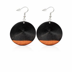 May include: A pair of circular earrings with a two-tone design. The top section is black, and the bottom is a warm brown. The earrings have a silver-coloured hook for pierced ears. These earrings are a stylish accessory.