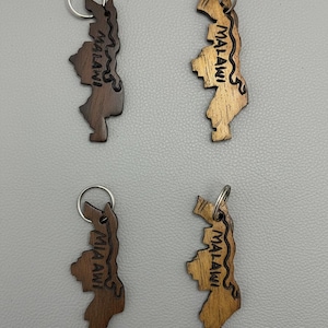 May include: Four wooden keychains shaped like the country of Malawi. Two are dark brown, and two are light brown. Each keychain has a silver keyring and the word "Malawi" engraved on it.