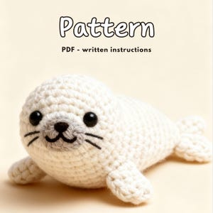May include: A crocheted white seal plushie with black eyes, gray nose, and black whiskers. The image includes the word "Pattern" and the text "PDF - written instructions". The seal is lying on a light beige background.