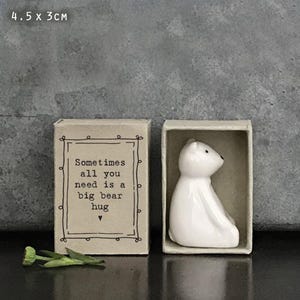 May include: A white ceramic bear figurine in a matchbox. The adjacent box has the text "Sometimes all you need is a big bear hug." The dimensions are 4.5 x 3 cm.