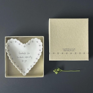 May include: A heart-shaped white dish with a scalloped edge and floral detailing, presented in a beige box. The dish is inscribed with the words "Grateful for so much, especially for you." A small sprig of greenery is also visible.