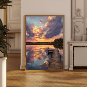May include: A framed landscape painting depicts a sunset over a lake. The sky is filled with vibrant orange, yellow, and purple clouds, reflected in the water. A wooden dock extends into the lake, with trees lining the far shore.
