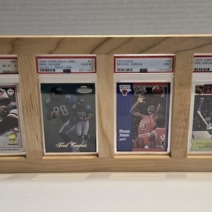 May include: A wooden frame displaying four graded sports cards. The cards feature Eddie Murray, Fred Taylor, Michael Jordan, and Phil Esposito. The frame is made of light-colored wood and is angled for display.