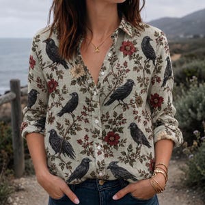 May include: A long-sleeve button-down shirt in a light beige color featuring a repeating pattern of black crows perched on branches with dark red and muted yellow flowers. The shirt has a classic collar and white buttons down the front placket.