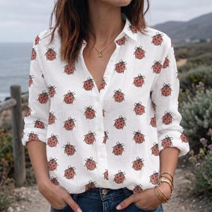 May include: A white long-sleeve button-down shirt featuring an all-over print of small red ladybugs with black spots. The shirt has a classic collar, a front button placket, and long sleeves with cuffs that are rolled up to the mid-forearm.
