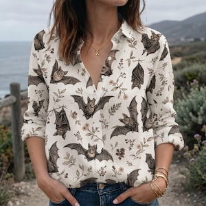 Peut inclure: Une chemise à manches longues boutonnée de couleur blanc cassé avec un motif répétitif de chauves-souris brunes et de petites tiges botaniques. La chemise présente un col classique, une patte de boutonnage et des manches longues avec poignets.