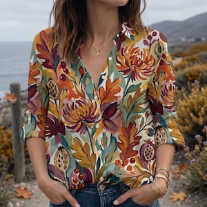 May include: A long-sleeved button-down shirt featuring a vibrant botanical print with orange, burgundy, and sage green floral and leaf motifs. The shirt has a classic collar, a front button placket, and is worn tucked into blue denim jeans.
