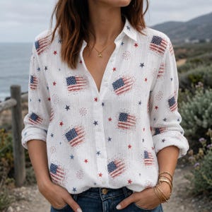 May include: A white long-sleeve button-down shirt featuring a repeating pattern of small American flags, red and blue stars, and firework-like bursts. The shirt has a classic collar, a front button placket, and long sleeves with rolled cuffs.