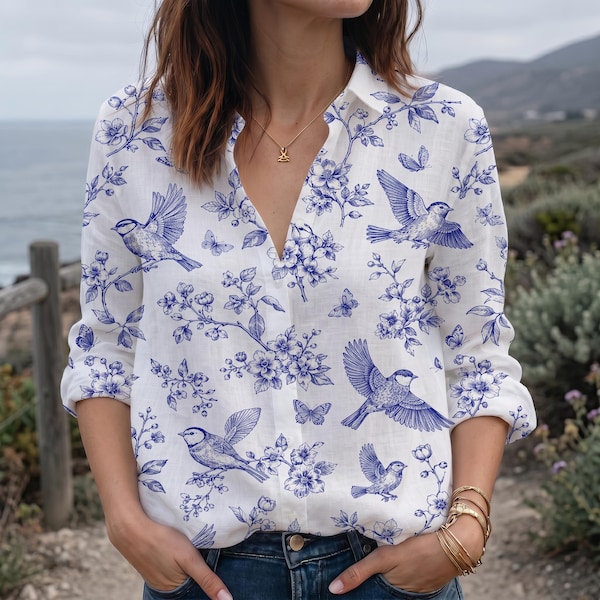 May include: A long-sleeved white button-down shirt featuring a blue botanical print with illustrations of birds and butterflies. The shirt has a V-neckline, a classic collar, and a repeating pattern of floral branches, flying birds, and small butterflies.