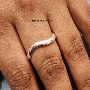 May include: A silver-colored ring with a wavy design. The ring is smooth and shiny, reflecting light. The text "SILVERARTGIFT25" is visible in the background. This ring is a piece of jewelry.