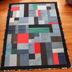 May include: A patchwork quilt made from denim fabric in shades of blue, black, and red. The quilt is made up of squares and rectangles of different sizes, and some of the squares have pockets. The quilt is bordered with a black fabric.