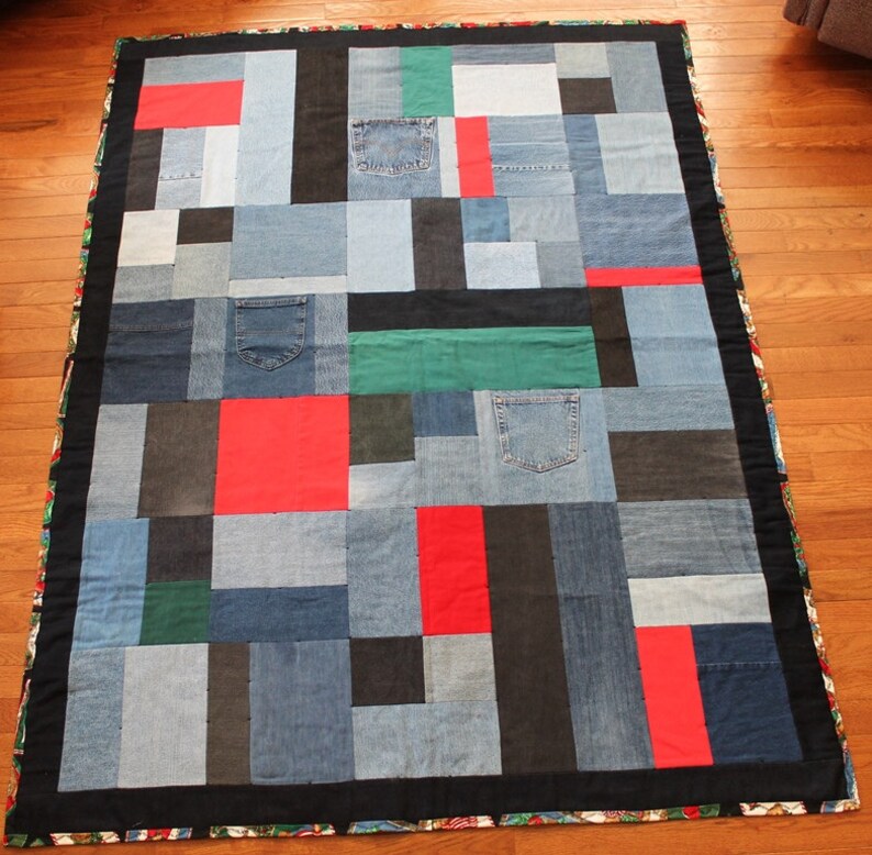 May include: A patchwork quilt made from denim fabric in shades of blue, black, and red. The quilt is made up of squares and rectangles of different sizes, and some of the squares have pockets. The quilt is bordered with a black fabric.