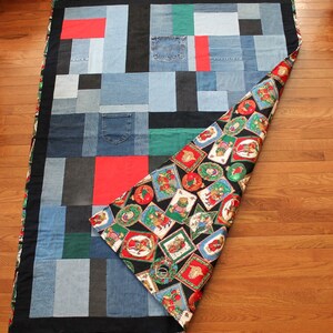 May include: A patchwork quilt made from denim fabric with a black border. The quilt is folded in half, revealing a black and red fabric with a pattern of Christmas ornaments and teddy bears.
