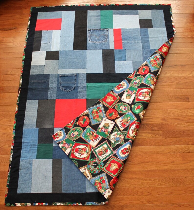May include: A patchwork quilt made from denim fabric with a black border. The quilt is folded in half, revealing a black and red fabric with a pattern of Christmas ornaments and teddy bears.