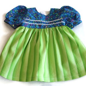 May include: A baby dress featuring a blue floral patterned bodice and short puffed sleeves. The bodice is trimmed with white. The skirt is bright green with vertical stripes. The dress is made of soft fabric.