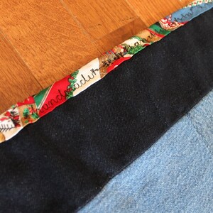 May include: A close-up of a black fabric with a colorful patterned trim. The trim features a repeating design of red, green, and white with the words "handmade" written in black.