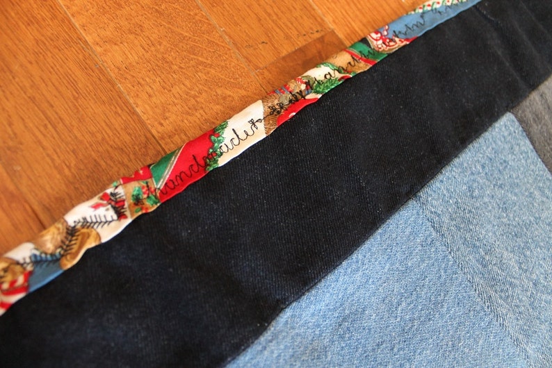 May include: A close-up of a black fabric with a colorful patterned trim. The trim features a repeating design of red, green, and white with the words "handmade" written in black.