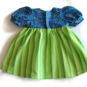 May include: A child's dress featuring a blue floral bodice and short, puffed sleeves. The skirt is a vibrant green with vertical stripes. The dress is made of cotton fabric and is designed for a young child.