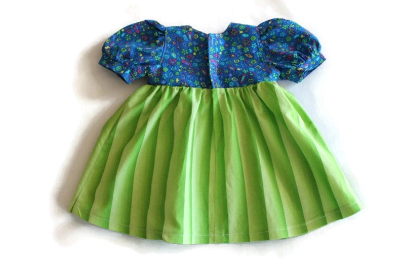 May include: A child's dress featuring a blue floral bodice and short, puffed sleeves. The skirt is a vibrant green with vertical stripes. The dress is made of cotton fabric and is designed for a young child.