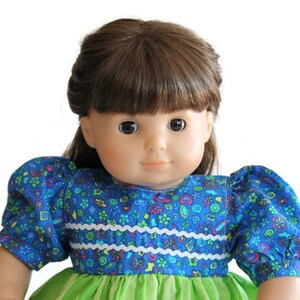 May include: A doll with brown hair and brown eyes, wearing a blue floral print dress with puffy sleeves and a green skirt. The dress has white trim across the bodice.