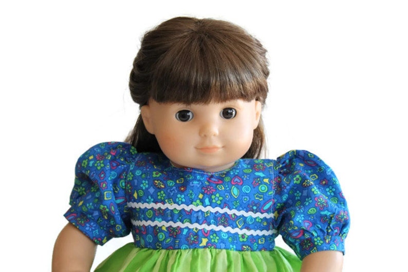 May include: A doll with brown hair and brown eyes, wearing a blue floral print dress with puffy sleeves and a green skirt. The dress has white trim across the bodice.