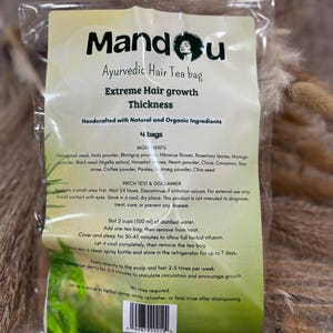 Puede incluir: Un paquete transparente de bolsas de té capilar ayurvédico Mandou. La etiqueta dice "Crecimiento Extremo del Cabello" y enumera ingredientes naturales. El paquete contiene 4 bolsas e incluye instrucciones de uso. El fondo presenta plantas secas.