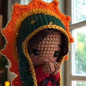 Peut inclure: Poupée au crochet faite à la main représentant la Vierge Marie, avec une robe rouge, des bordures vertes et dorées, et une auréole en forme de soleil. Le visage de la poupée est détaillé et elle est en position de prière. Un ruban noir orne la robe.