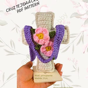 Puede incluir: Una cruz tejida a crochet con flores rosas y amarillas, detalles morados y el texto "CRUZ TEJIDA A CROCHET PDF PATTERN." La cruz mide aproximadamente 17 cm de alto. El diseño incluye el texto "Nivel: principiante" y "Medida: 17cm."