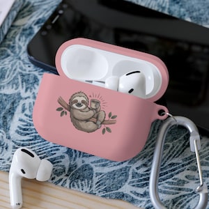 May include: A pink AirPod case with a cartoon sloth illustration holding a cup of coffee. The case is open, revealing white AirPods inside. A silver carabiner clip is attached to the case.