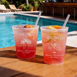Puede incluir: Dos vasos de pl&aacute;stico transparente llenos de l&iacute;quido rosa, hielo y rodajas de fruta, cada uno con un dise&ntilde;o impreso en blanco. El texto dice THE BACH Club, EST. 2026, Martin's Bachelorette, NEW YORK, NY, con ilustraciones de palmeras, una copa de martini y sandalias.