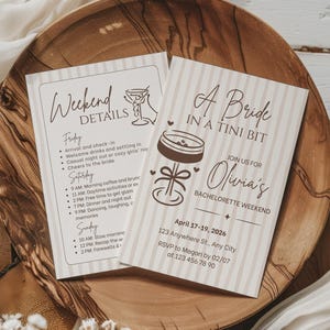 Könnte beinhalten: Zwei Einladungskarten auf einem Holztablett. Eine Karte lautet "Weekend Details" mit einer Liste von Aktivitäten. Die andere Karte lautet "A Bride in a Tini Bit" mit Veranstaltungsdetails, einschließlich Datum, Ort und RSVP-Informationen.