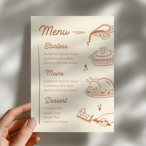 May include: A beige menu card with the word "Menu" at the top, listing starters, mains, and dessert options. The menu includes Butternut Squash Soup, Cranberry Brie Bites, and Autumn Harvest Salad. Decorative illustrations of food items are included.