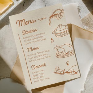 May include: A beige menu card with brown text and illustrations. The menu includes starters, mains, and dessert options. The illustrations include a teapot, a covered dish, a roasted turkey, and a hand holding a pie server.